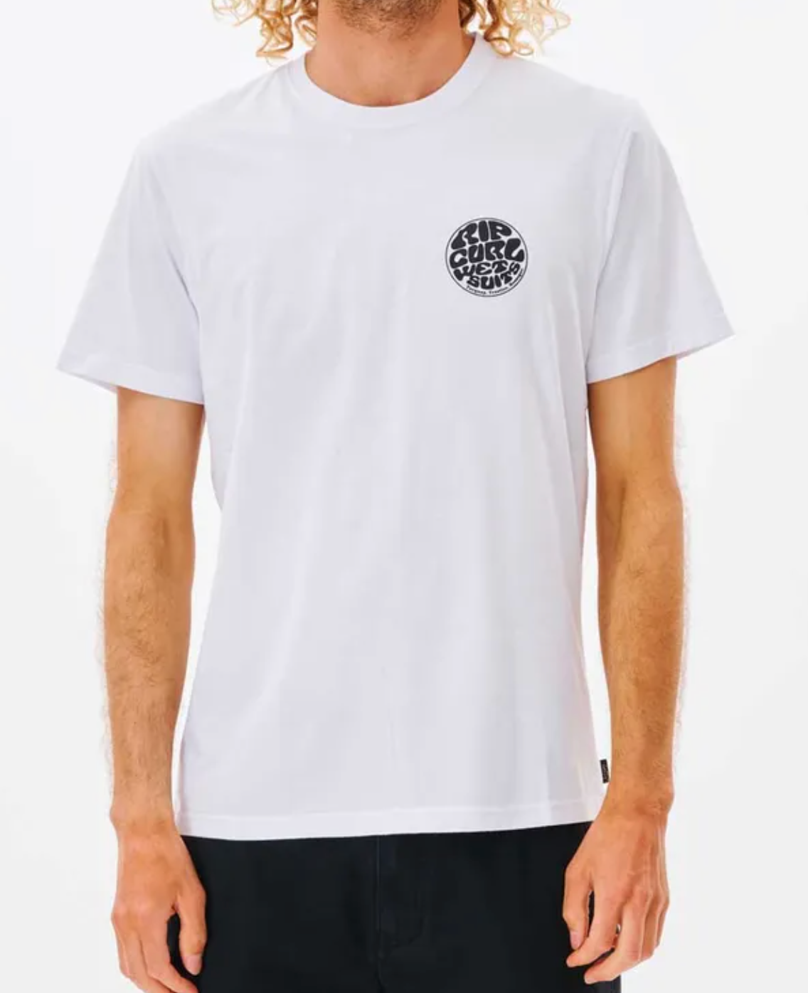 A person in a 100% cotton white Rip Curl Wetsuit Icon Tee with a circular "Soul Surf Supply" logo in stylized font. With curly blonde hair and black pants, they embody the perfect casual tee vibe against a plain white background.