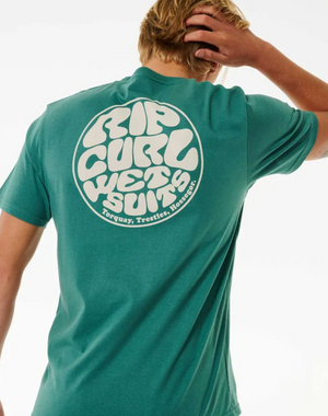 A person with blonde hair wears the Rip Curl Wetsuit Icon Tee, a comfy teal 100% cotton T-shirt featuring a large white circular logo on the back that reads "Torquay, Trestles, Hossegor," and holds their head with one hand.