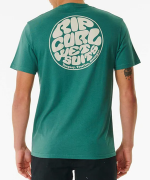A person wears the Rip Curl Wetsuit Icon Tee, a comfy 100% cotton green T-shirt with a large round logo on the back that states "Rip Curl Wetsuits Torquay, Trestles, Hossegor" in bold white. They have an arm tattoo and pair it with dark pants.