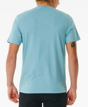 A person with blond hair, seen from the back, wears a light blue Rip Curl Big Mumma Icon Tee and black pants. An eye tattoo is visible on their left arm. The plain white background highlights the tee’s relaxed style.