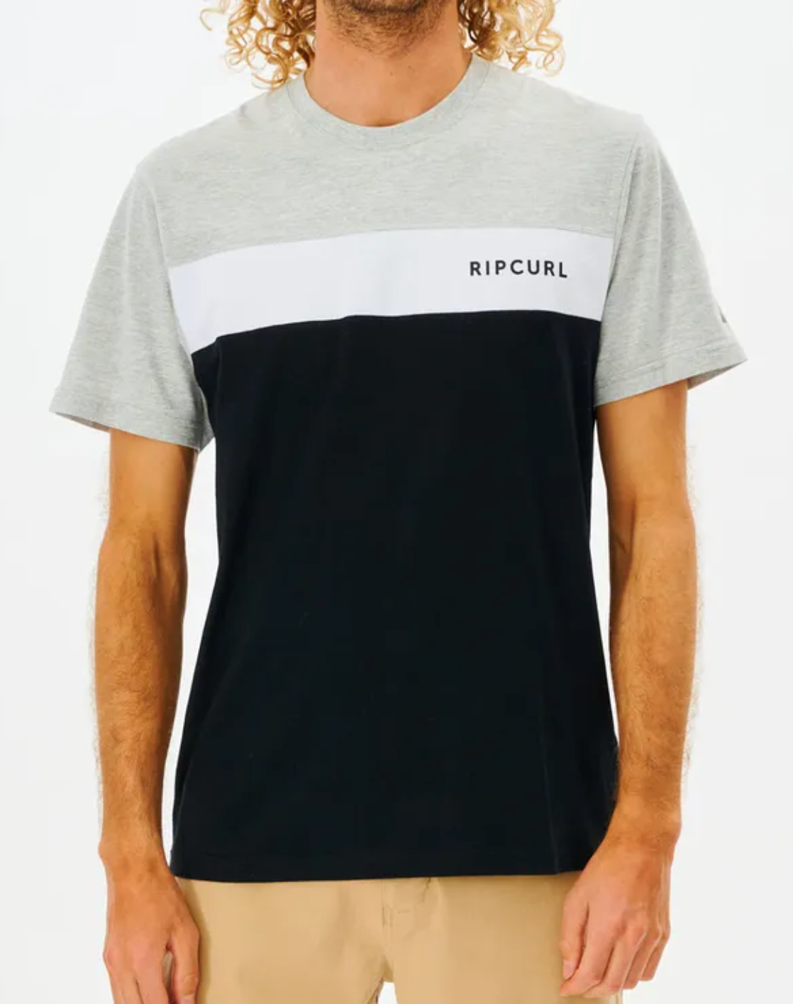 A person wearing the Rip Curl Undertow Panel Tee made of 100% cotton in gray, white, and black stands against a plain background. The casual tee features "RIP CURL" on the chest and is paired with beige pants.