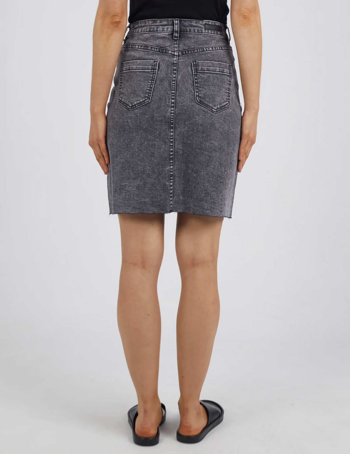 A person in a gray Foxwood Belle Skirt with an A-line fit and a black top stands, back to the camera, wearing black sandals against a plain, light backdrop.