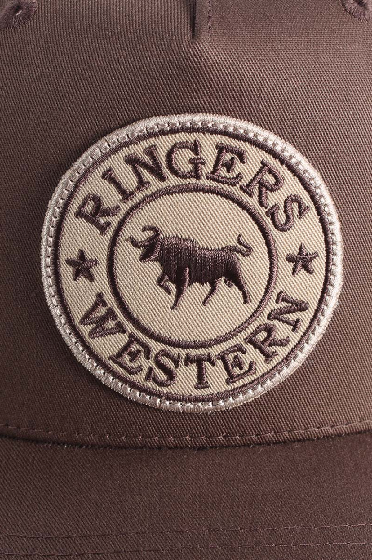 Close-up of the Ringers Western Signature Bull Trucker Cap, featuring a brown cotton twill patch with "RINGERS WESTERN" text, stars, and an embroidered bull in the center, stitched on a brown trucker cap with mesh back.