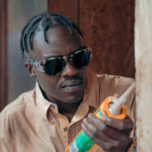 A person wearing SafeStyle Cruisers Milky Tort Frame Polarised Lens sunglasses and a beige shirt uses a caulking gun to apply sealant to a wooden surface.