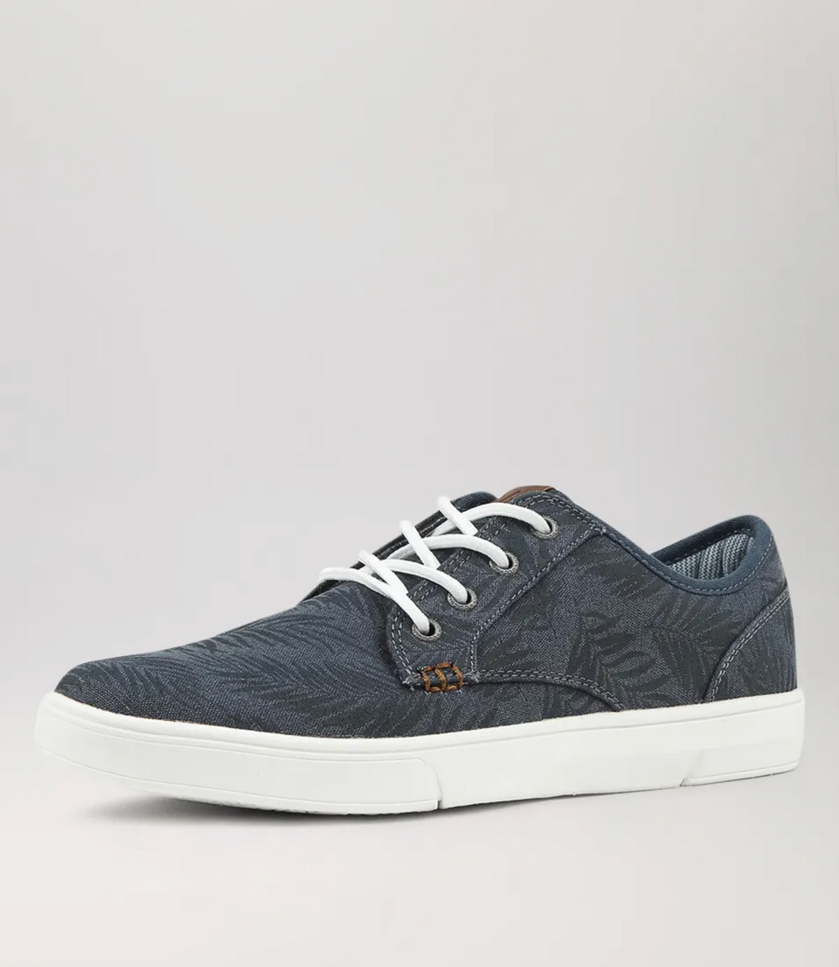 The Colorado Albatross Canvas Sneaker is navy blue with a subtle leaf pattern, white laces, and a white sole. It includes a memory foam inner sole for wide-fit comfort and is showcased against a plain gray background from a side angle.