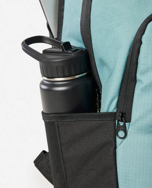 A close-up of a teal Rip Curl Ozone 2025 School 30L Backpack with a black zipper, featuring a black water bottle in the outer side pocket.