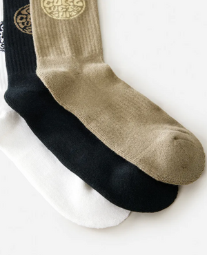 The Rip Curl Wetty Crew Sock 3 Pack includes three pairs—white, black, and olive green—in a soft acrylic blend. The olive green socks feature a circular gold design near the top for added style and comfort.