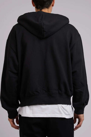 A person is seen from behind, dressed in a cozy and stylish Silent Theory Zip Hoodie in black, layered over a white shirt. The loose-fitting hoodie has its hood down and is composed of 80% cotton and 20% polyester. The individual also wears black pants, with hands partially visible at their sides against a plain background.