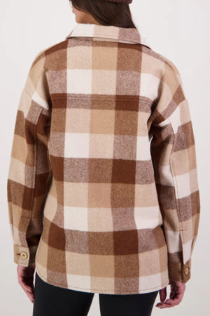 A person is seen from the back wearing a Swanndri Anchorage V3 Womens Wool Shacket in brown, beige, and cream plaid with long sleeves and buttoned cuffs, made from premium New Zealand wool, paired with black pants.