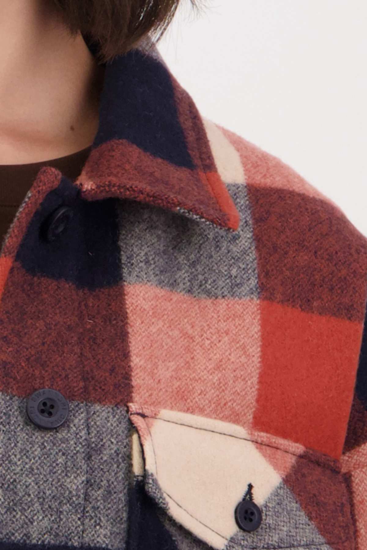 Close-up of someone wearing a Swanndri Anchorage v2 Wool Shirt Jacket with large red, navy, and beige checks. The wool complements the black buttons and front pocket. The person's neck is visible, enhancing the cozy merino blend look.