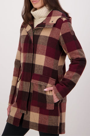 A woman wears a hooded, buttoned Swanndri Annmore V2 Wool Overcoat in large red, beige, and brown plaid over a cream turtleneck sweater, with her left hand in the coat pocket.