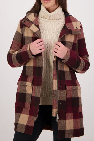 A woman in a beige turtleneck and a Swanndri Annmore V2 Wool Overcoat—long, plaid in burgundy, brown, and tan with large front pockets and a zipper—stands against a light background.