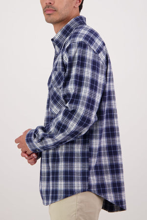 A person wears the Swanndri Barn Shirt in blue and white plaid with beige pants, standing sideways against a plain light background—a classic heritage look ideal for winter layering.