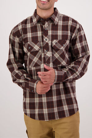 A person wearing a brown and white plaid Swanndri Barn Shirt with tan pants stands against a plain background, smiling with hands clasped—ideal for heritage style or easy winter layering.