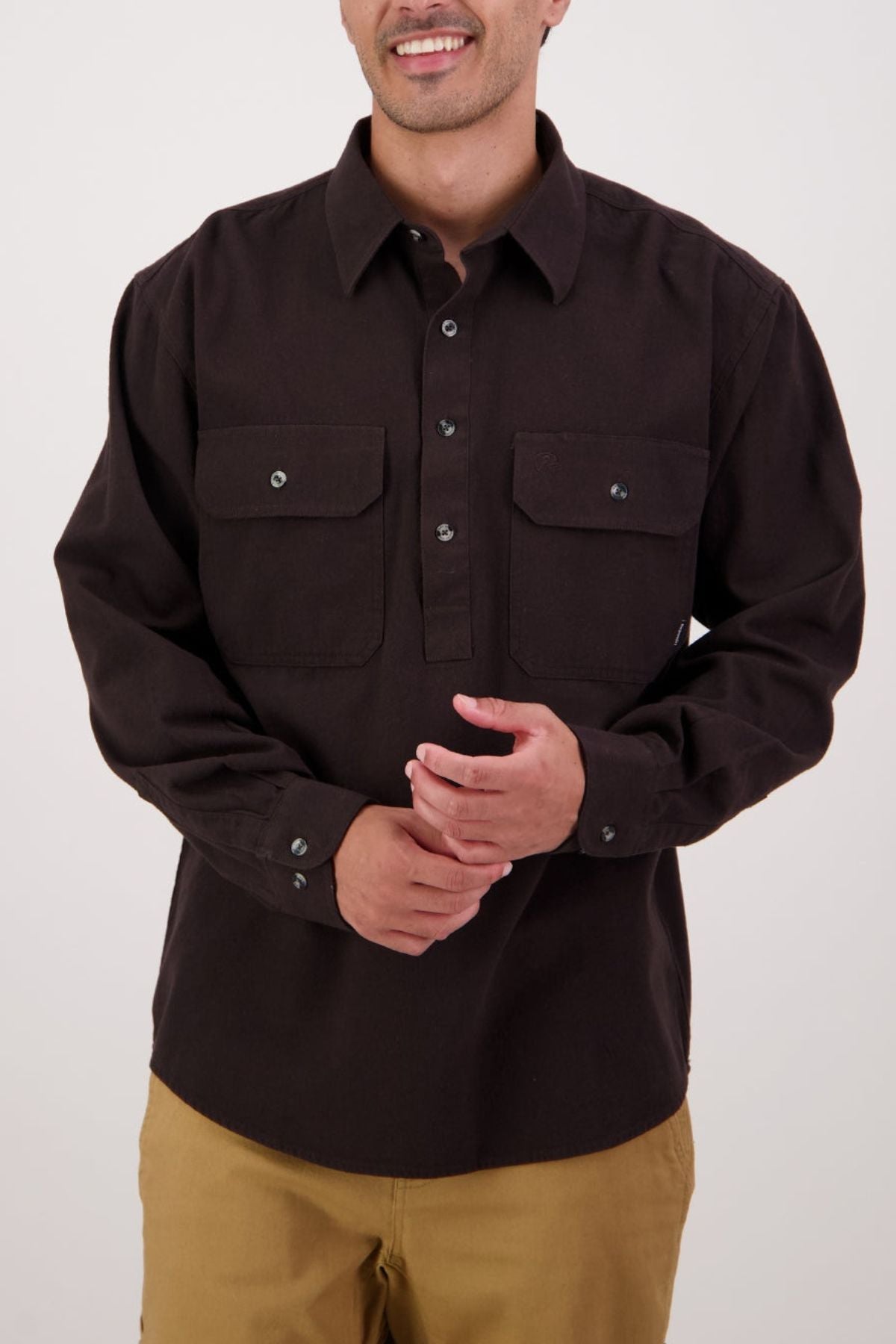 Wearing the Swanndri Barn Shirt in dark brown with two chest pockets and light brown pants, this look against a plain background is ideal for winter layering and highlights the shirt’s timeless heritage style.