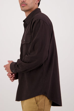 A person in a dark brown Swanndri Barn Shirt and light tan pants, facing left with bent arms, shown from mid-thigh up against a plain light background—combining classic heritage style for ideal winter layering.