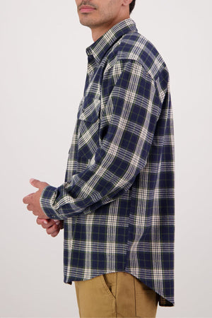 A person in a blue and white plaid Swanndri Barn Shirt and tan pants is shown from the side against a plain light background, with only their upper body and part of their face visible, showcasing this classic winter layering piece.