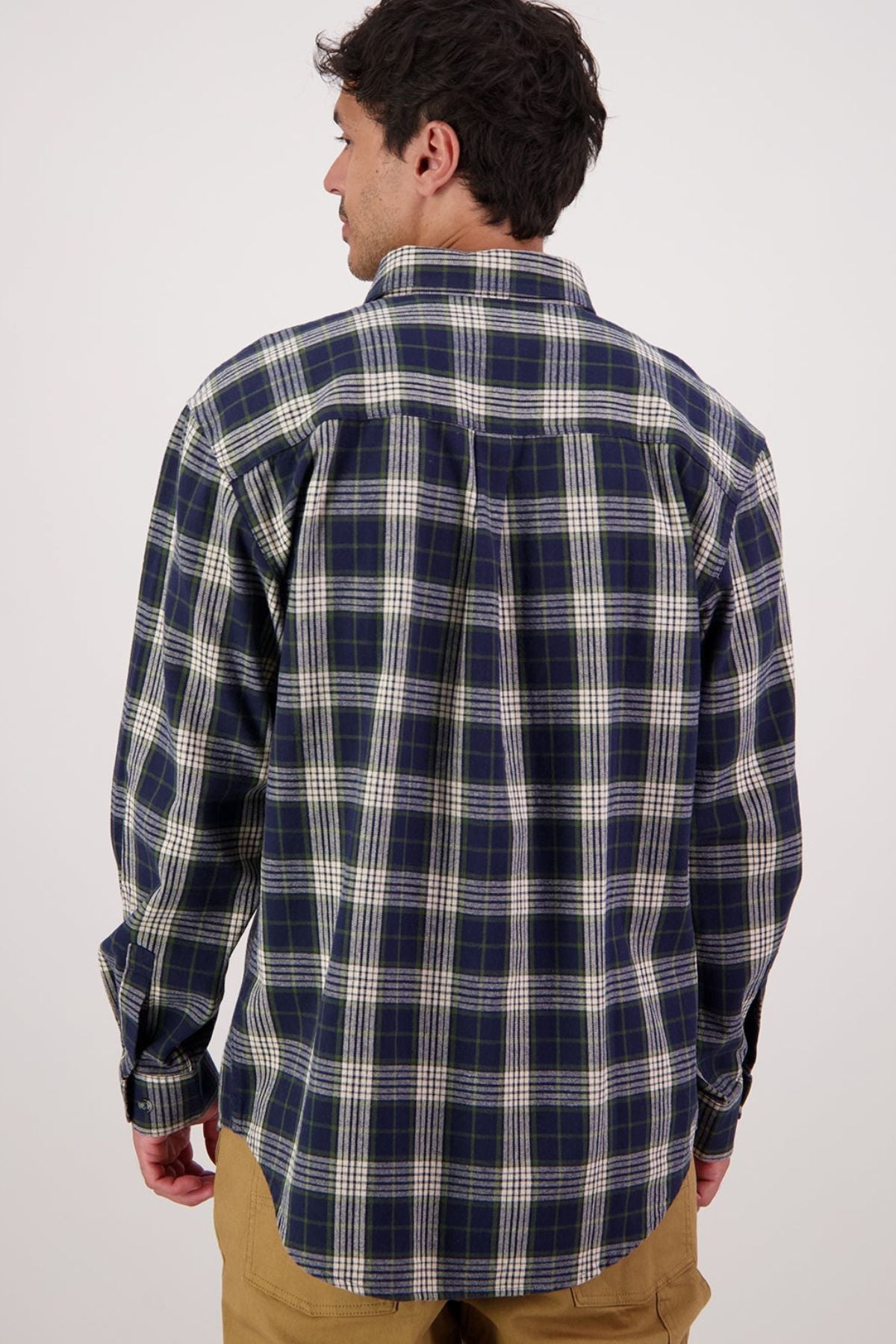 A man in the Swanndri Barn Shirt (blue, green, and white) and tan pants stands with his back to the camera against a plain light background, highlighting this classic heritage piece ideal for winter layering.