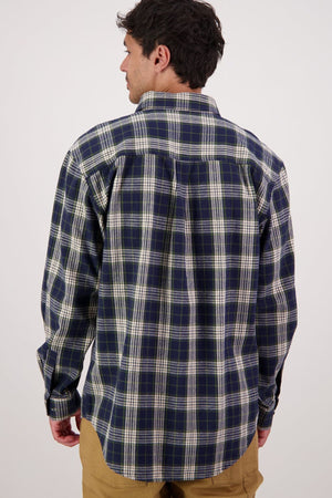 A man in the Swanndri Barn Shirt (blue, green, and white) and tan pants stands with his back to the camera against a plain light background, highlighting this classic heritage piece ideal for winter layering.
