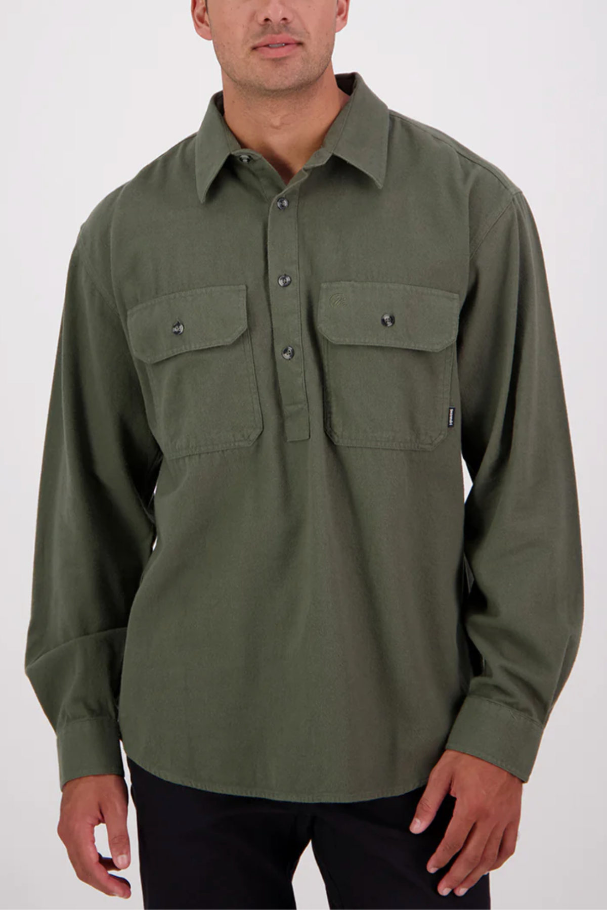 A man wearing a Swanndri Barn Shirt—relaxed fit, long-sleeved, olive green 100% cotton with two chest pockets—stands against a plain light background.