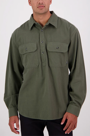 A man wearing a Swanndri Barn Shirt—relaxed fit, long-sleeved, olive green 100% cotton with two chest pockets—stands against a plain light background.