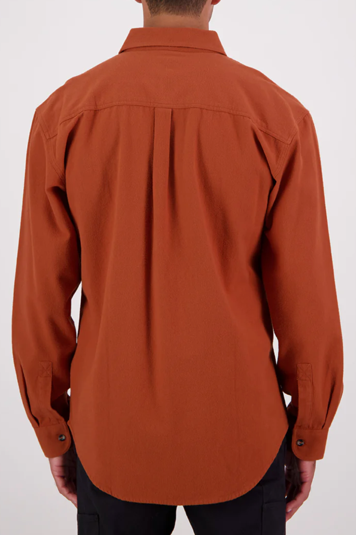 A person stands facing away, wearing a rust-colored Swanndri Barn Shirt in a relaxed fit made from 100% cotton, paired with black pants against a plain light background.