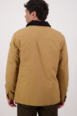 A man with short dark hair, seen from behind, wears a Swanndri Barrytown V3 Canvas Jacket with a black collar and dark pants. His arms are relaxed at his sides as he stands against a plain light background.