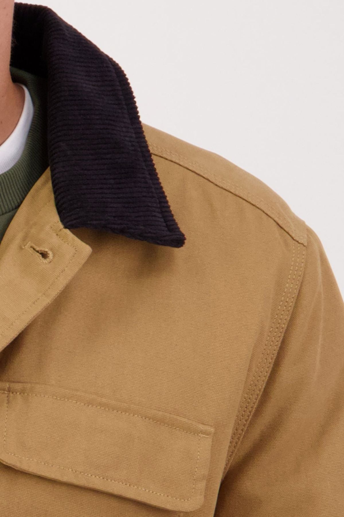 Close-up of a person wearing the Swanndri Barrytown V3 Canvas Jacket, featuring a black corduroy collar and green shirt underneath. Only part of the cotton canvas shoulder and chest is visible.