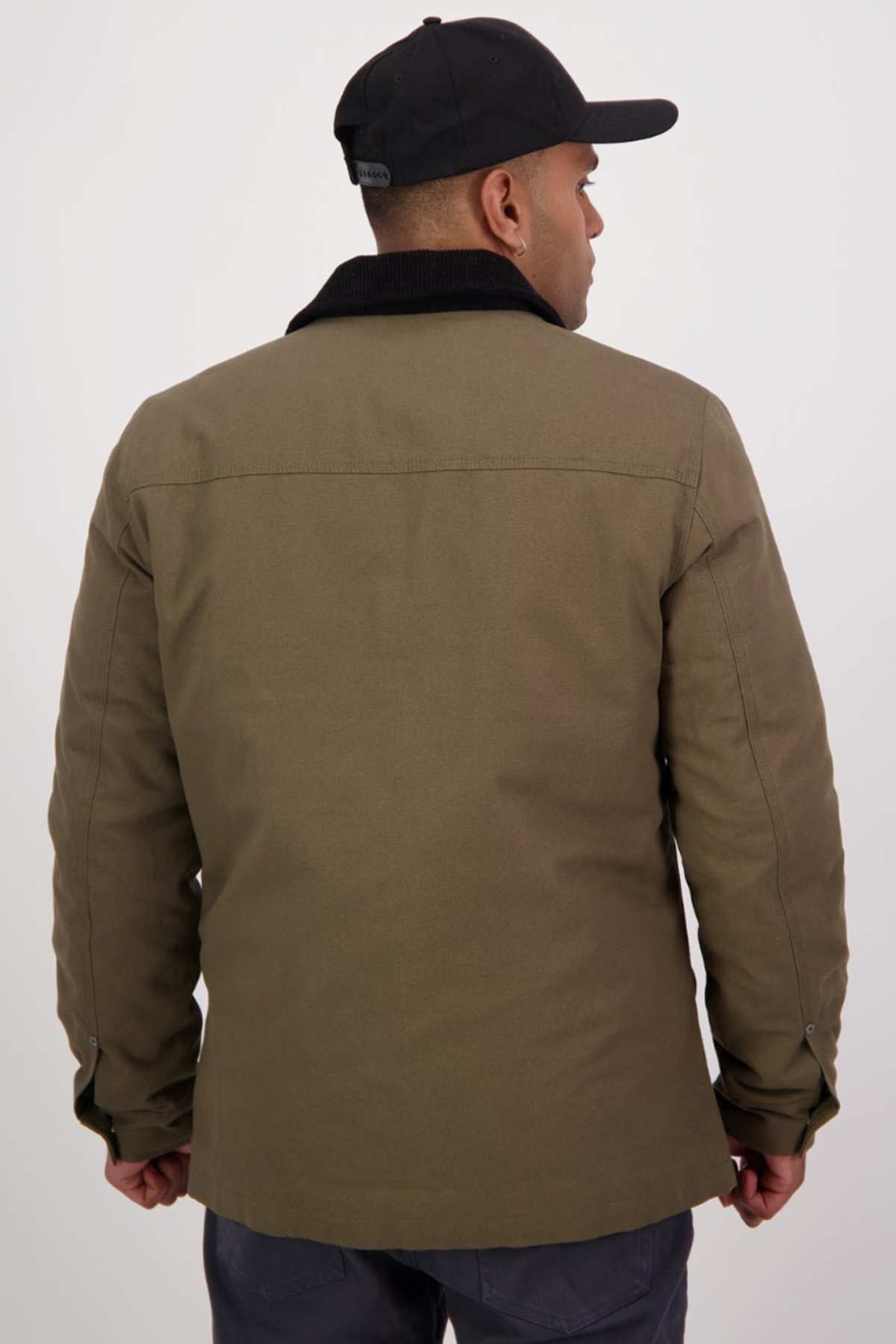 A person in a Swanndri Barrytown v3 Canvas Work Jacket and a black cap is facing away from the camera. The quilted insulated jacket, featuring a dark collar and buttoned cuffs, stands out against a plain white background.