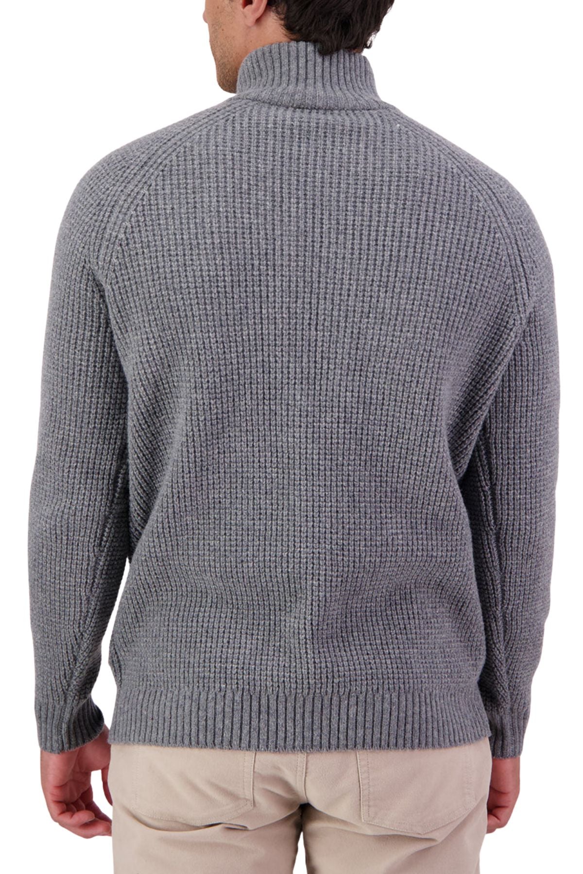 A man is pictured from the back wearing the Swanndri Chalky Island Waffle Jumper—a chunky gray knit sweater with a high collar, ribbed texture, and long sleeves—paired with light beige pants for a cozy look.