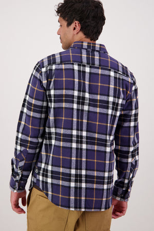 A man, seen from behind, wears a Swanndri Crofton Shirt—purple, black, and white plaid in 100% cotton with long sleeves—paired with tan pants, evoking classic heritage workwear against a plain light background.