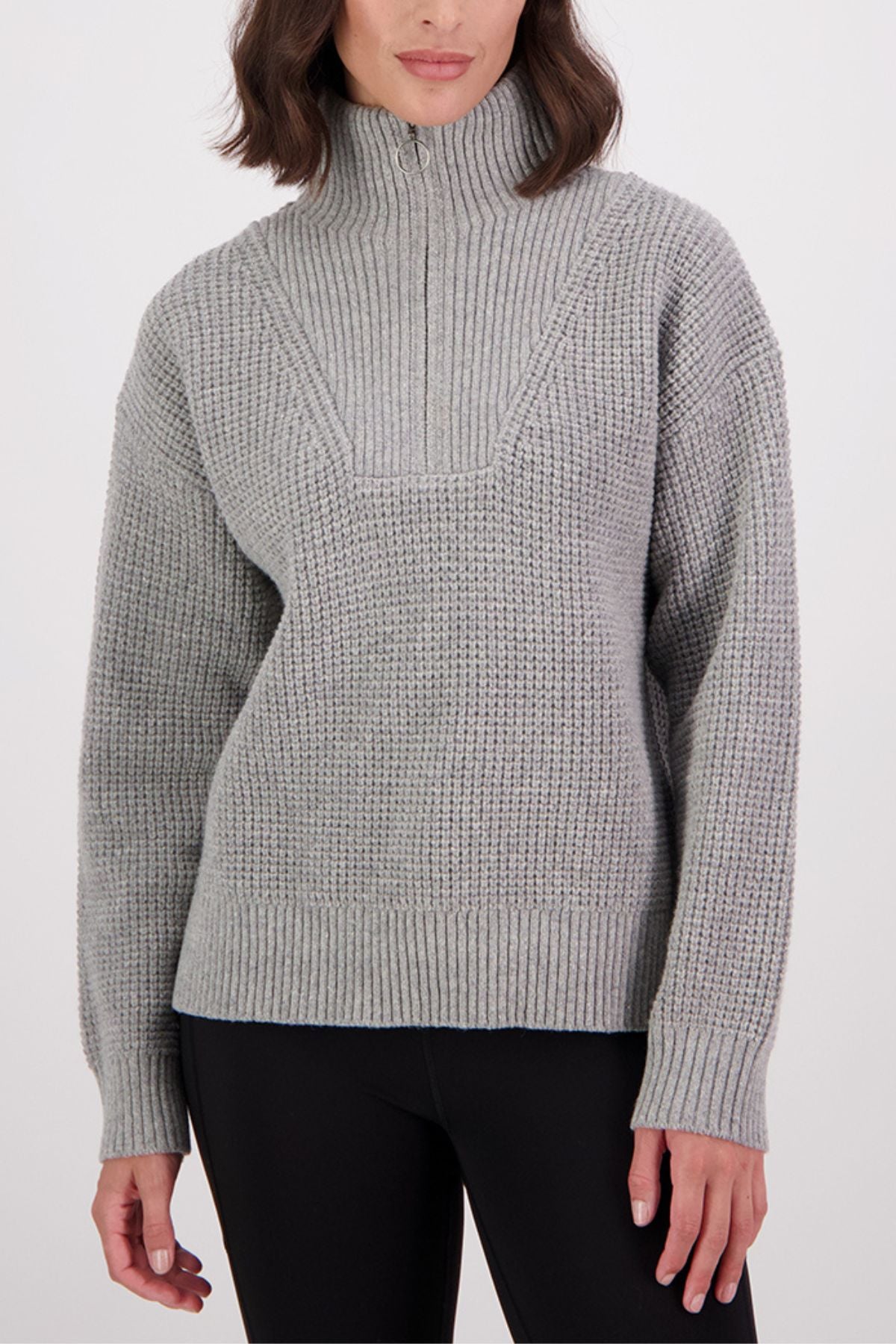 A woman models the Swanndri Darlinghurst Zip Jumper, a light gray lambswool knit with an oversized collar, front zip, and ribbed cuffs and hem, styled with black leggings. The image captures her from shoulders to hips.