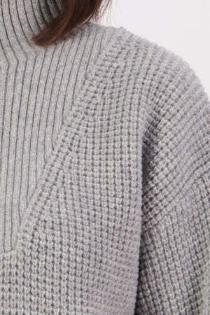 Close-up of a person wearing the Swanndri Darlinghurst Zip Jumper in light gray lambswool over a ribbed turtleneck, highlighting both textures. Only the shoulder, neck, and hair are partially visible.