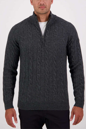 A man in a dark gray Swanndri Doncaster v2 Zip Cable Knit sweater over a white shirt stands against a plain white background.