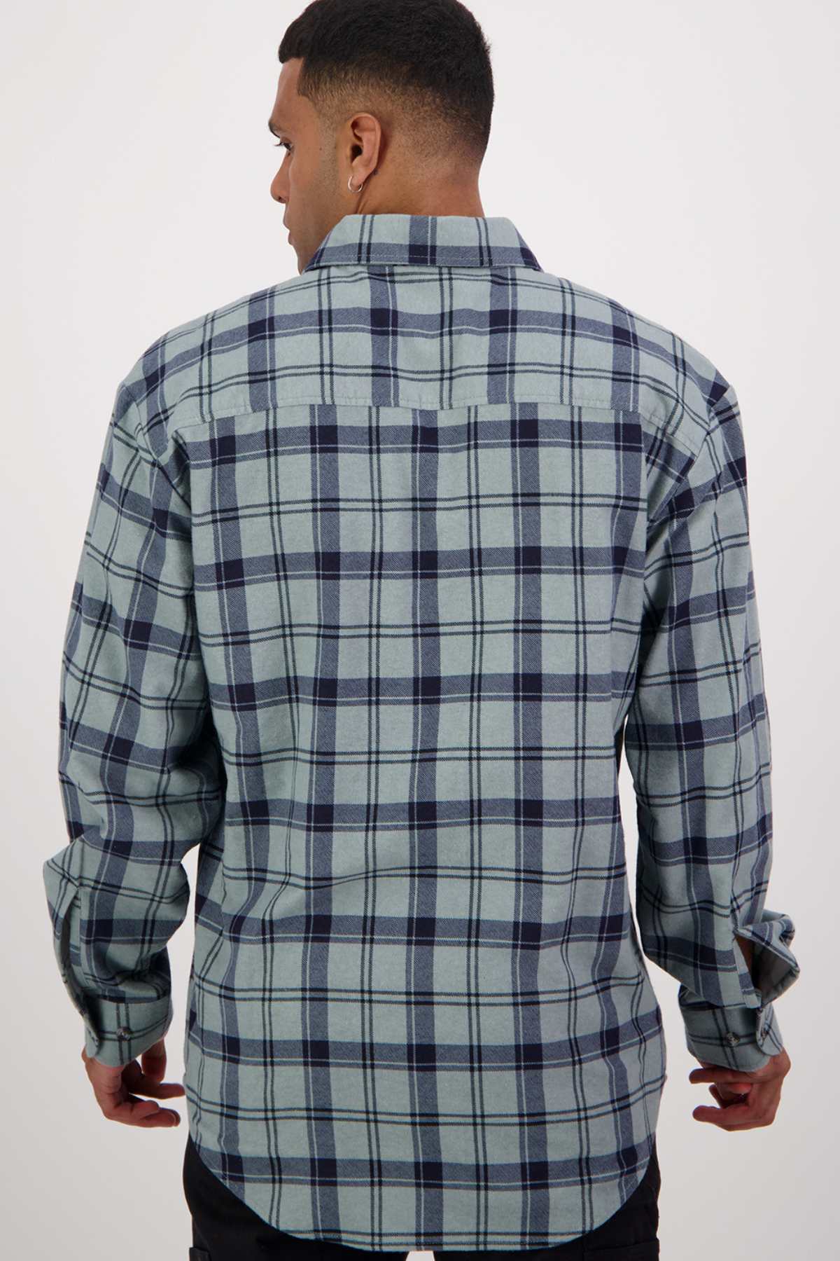 A man is seen from the back wearing a green and navy blue plaid long sleeve shirt from the Swanndri Egmont Flannelette Twin Pack. He has short hair and is standing against a plain white background.