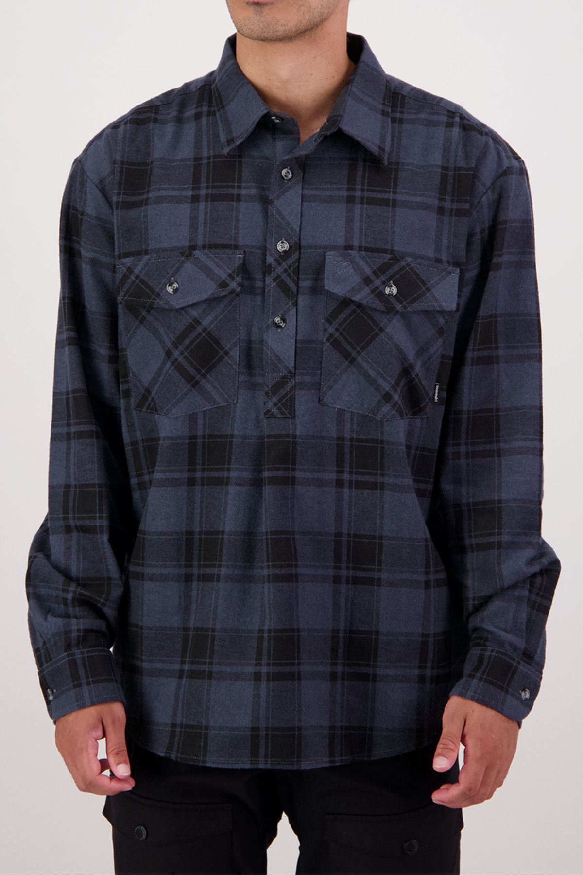 A person wearing the Swanndri Egmont Flannelette Twin Pack—featuring a long-sleeve, dark blue and black plaid heavy flannelette shirt with two chest pockets—stands against a plain background, face not visible.