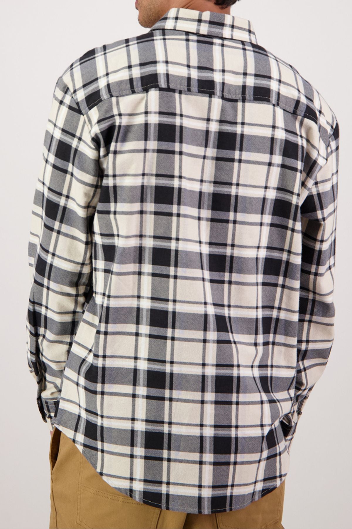 A person is shown from the back wearing an untucked Swanndri Egmont Flannelette shirt in a black, white, and gray plaid. The heavy brushed cotton long-sleeve shirt is paired with tan pants.