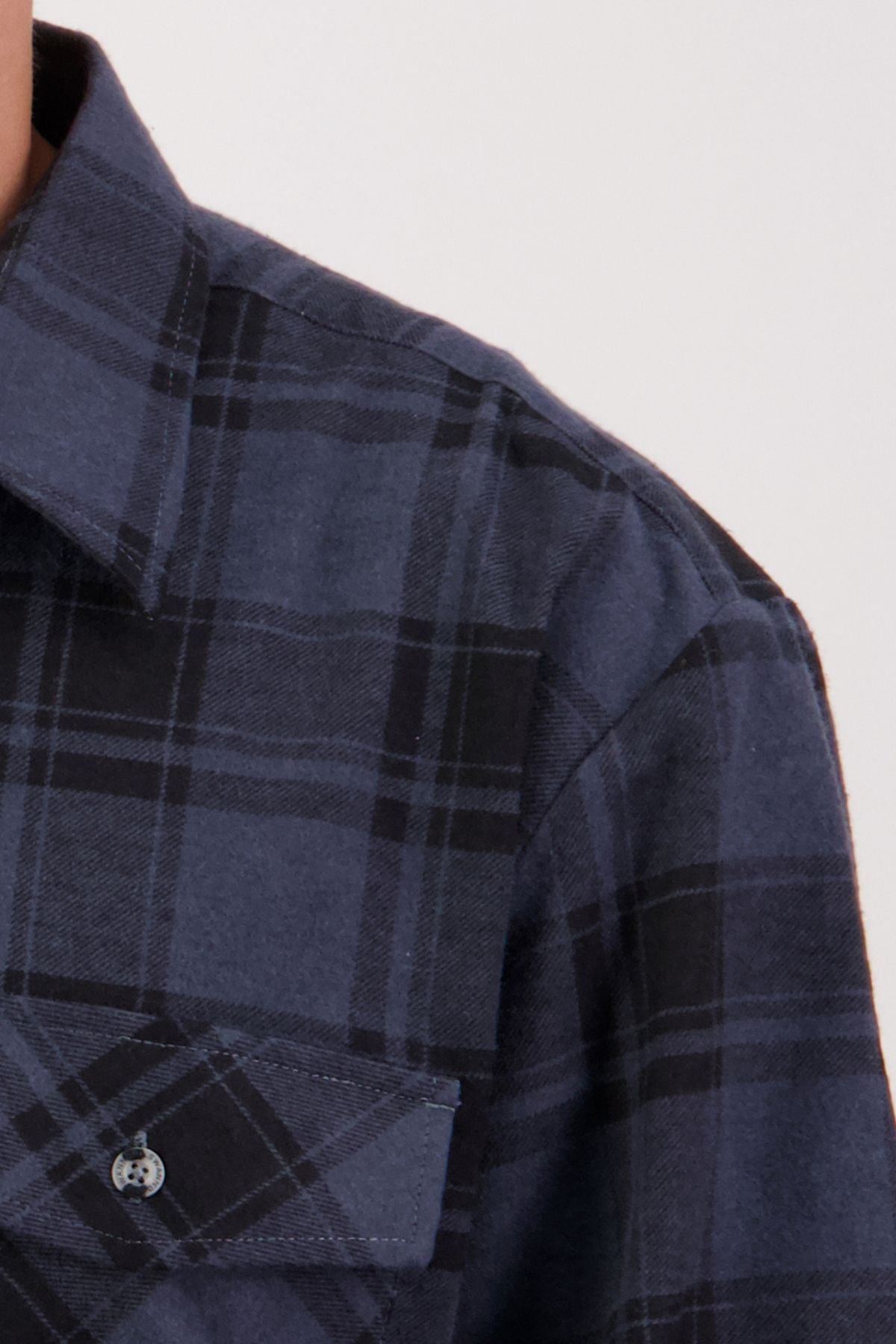 A close-up of someone wearing the Swanndri Egmont Flannelette Twin Pack shirt in blue and black plaid, featuring a front pocket and buttoned collar, shown from shoulder to chest.