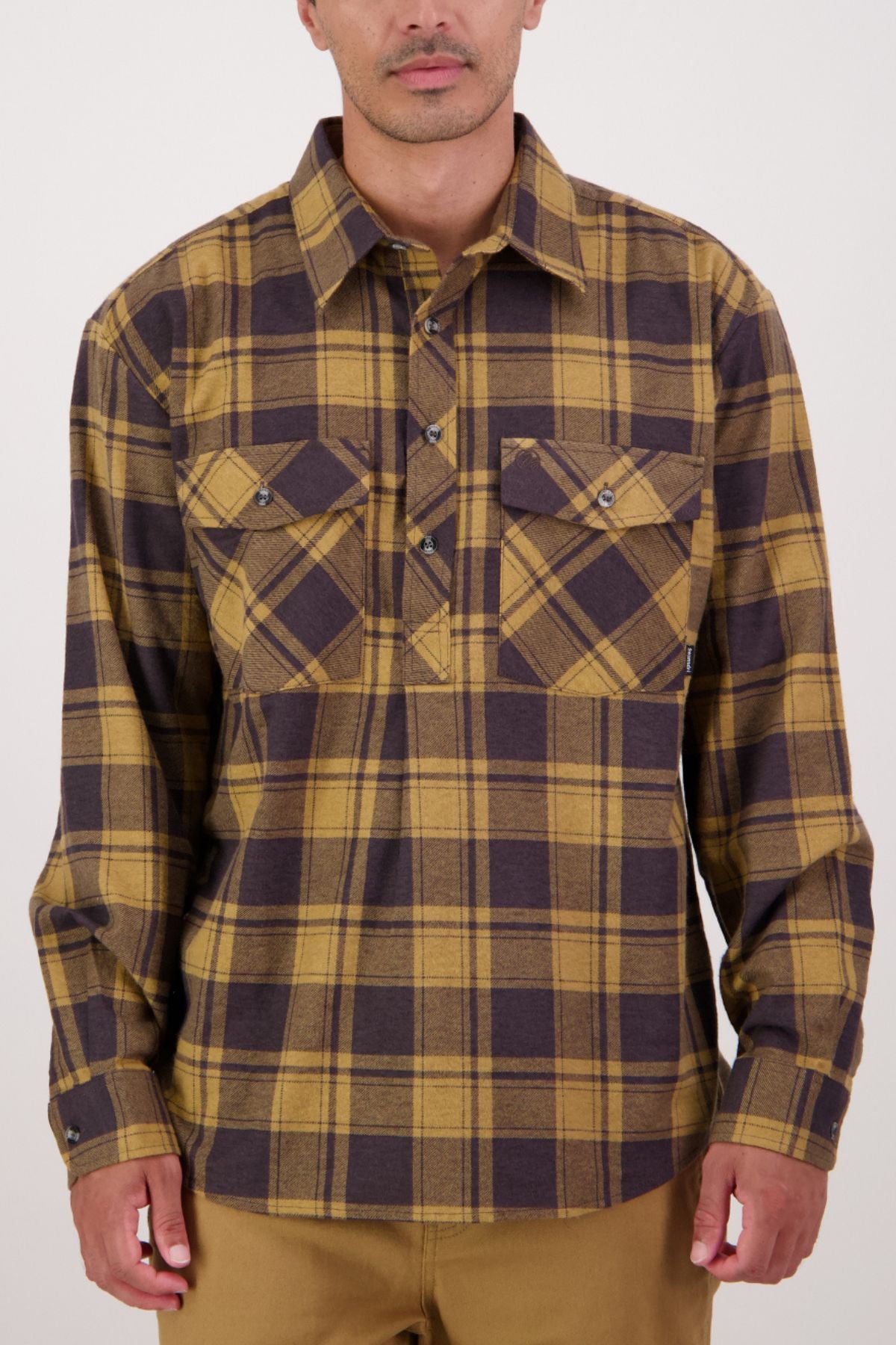A man wears a Swanndri Egmont Flannelette Twin Pack shirt in yellow and brown plaid with two chest pockets, standing against a plain light background.