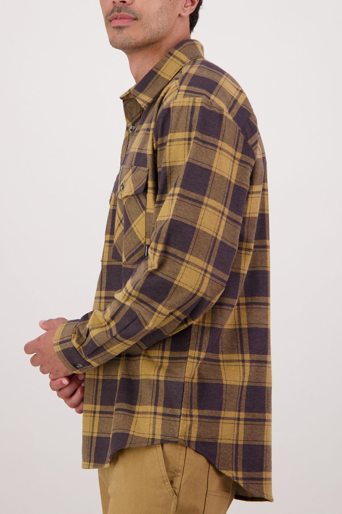 A man stands in profile against a light background, wearing a Swanndri Egmont Flannelette Twin Pack yellow and brown plaid long sleeve shirt with a chest pocket.