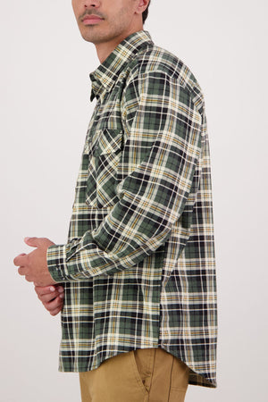 A man wearing a Swanndri Egmont Flannelette Twin Pack shirt in green, white, and yellow plaid with tan pants stands in profile against a plain white background.