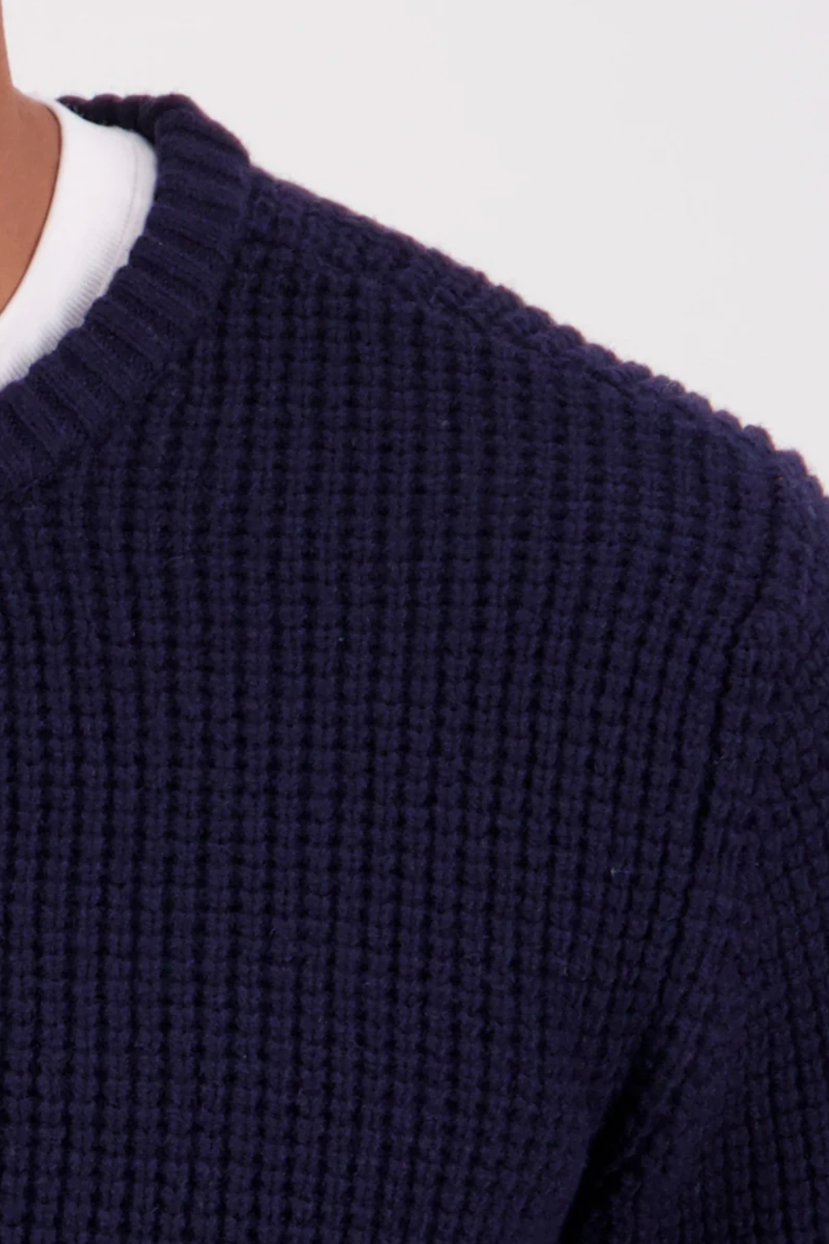 Close-up of the Swanndri Fistral Waffle Knit in navy blue, layered over a white shirt. The image focuses on the textured waffle pattern at the shoulder and neck against a light background.
