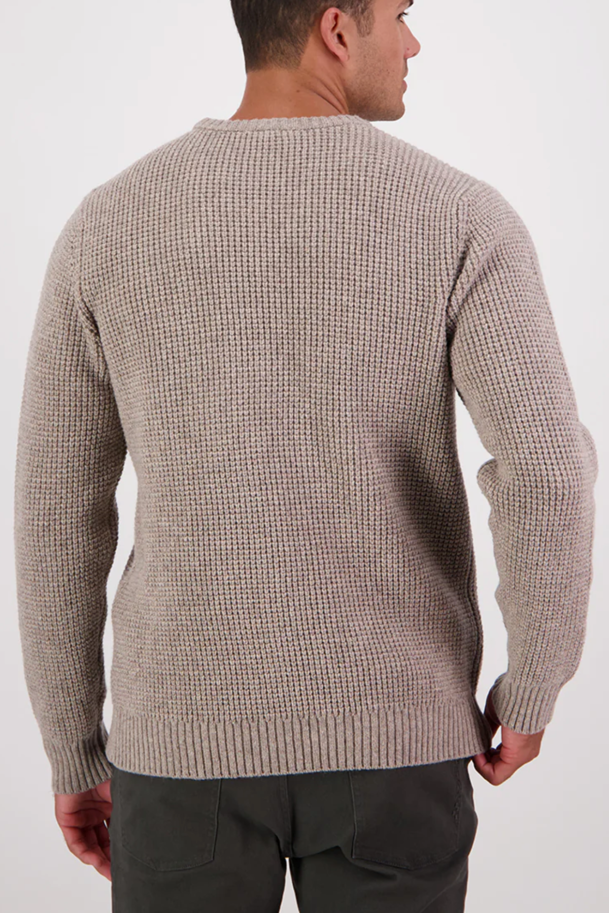 A man is shown from the back wearing the Swanndri Fistral Waffle Knit sweater in light beige, featuring a classic waffle design and ribbed cuffs, paired with dark pants against a plain white background.