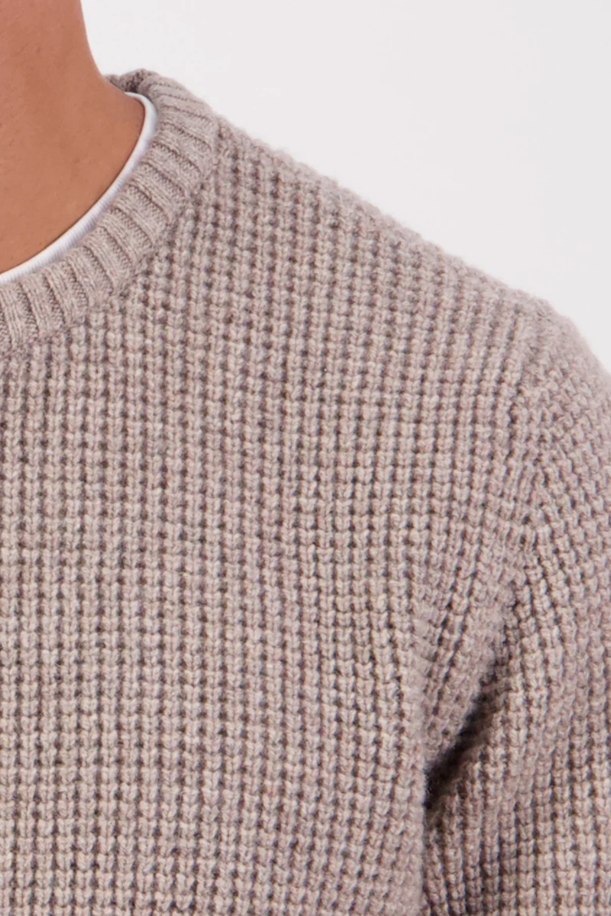 Close-up of a person wearing the Swanndri Fistral Waffle Knit sweater in beige, featuring a ribbed crew neck and layered over a white shirt. Only the shoulder and part of the chest are shown against a plain background.