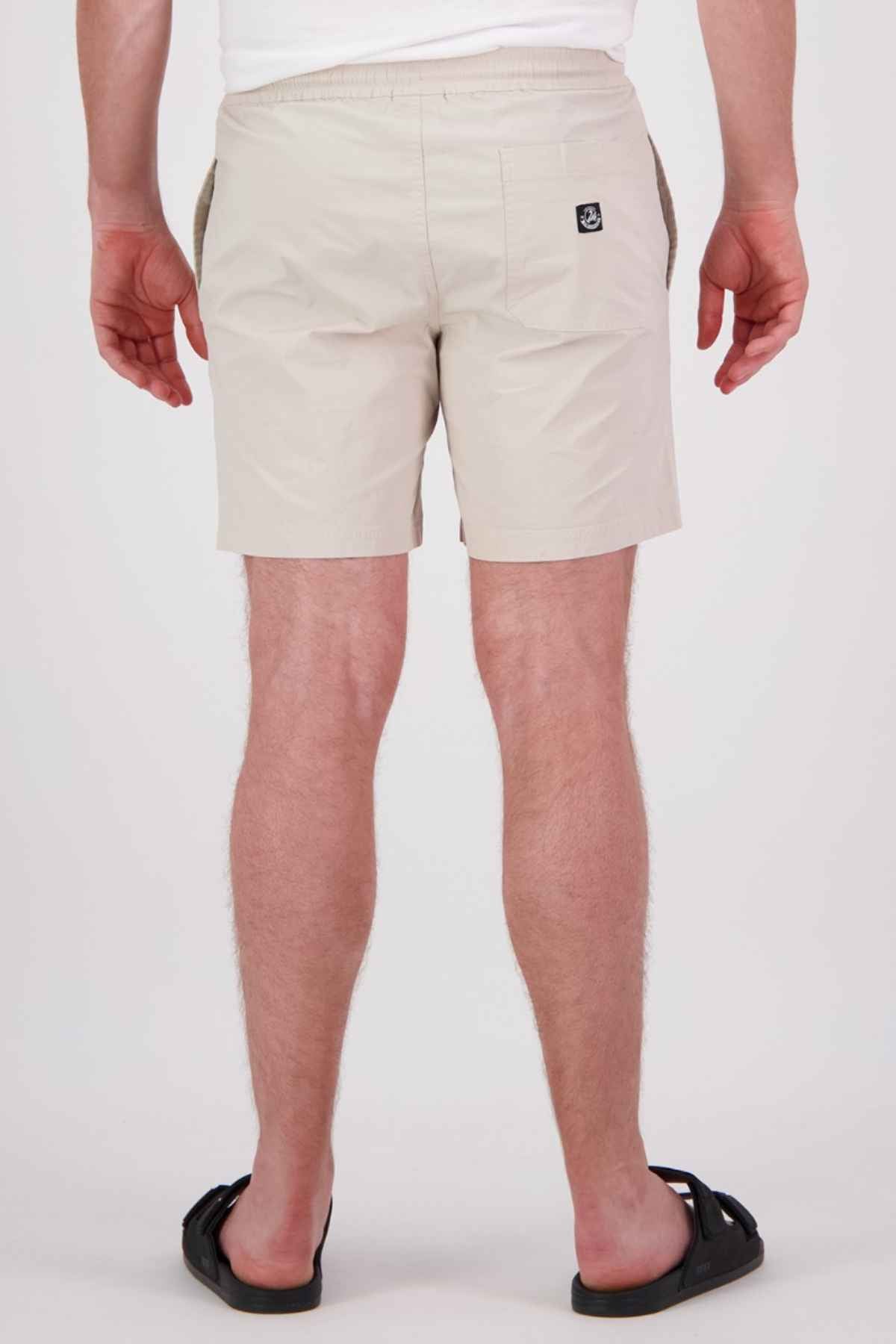A rear view of a person wearing the Swanndri Frankton Short with an elastic waist, paired with a white shirt and black sandals, standing against a plain background.