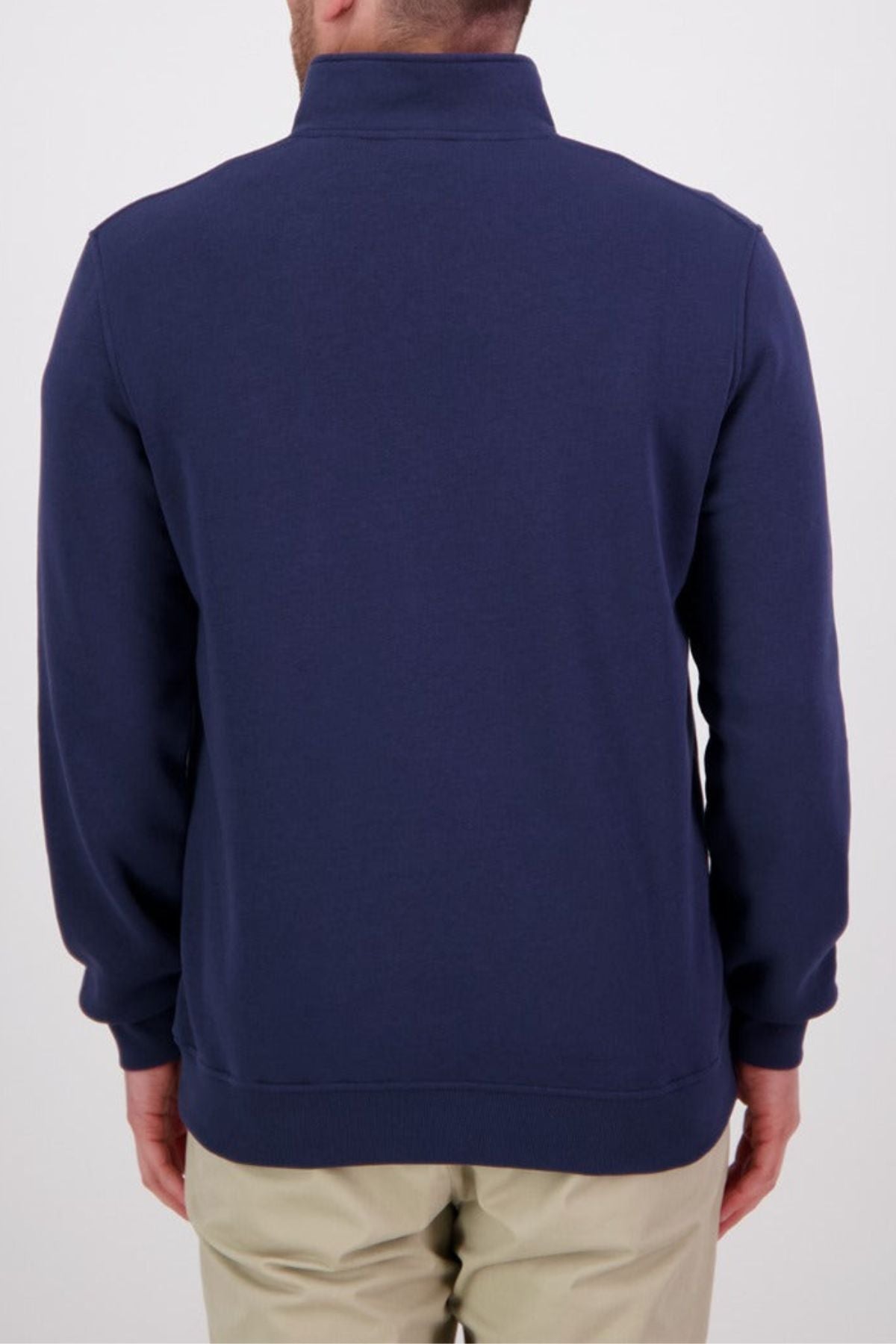 A man is seen from the back, wearing a navy Swanndri Fundamentals Quarter Zip and light beige pants, standing against a plain white background.