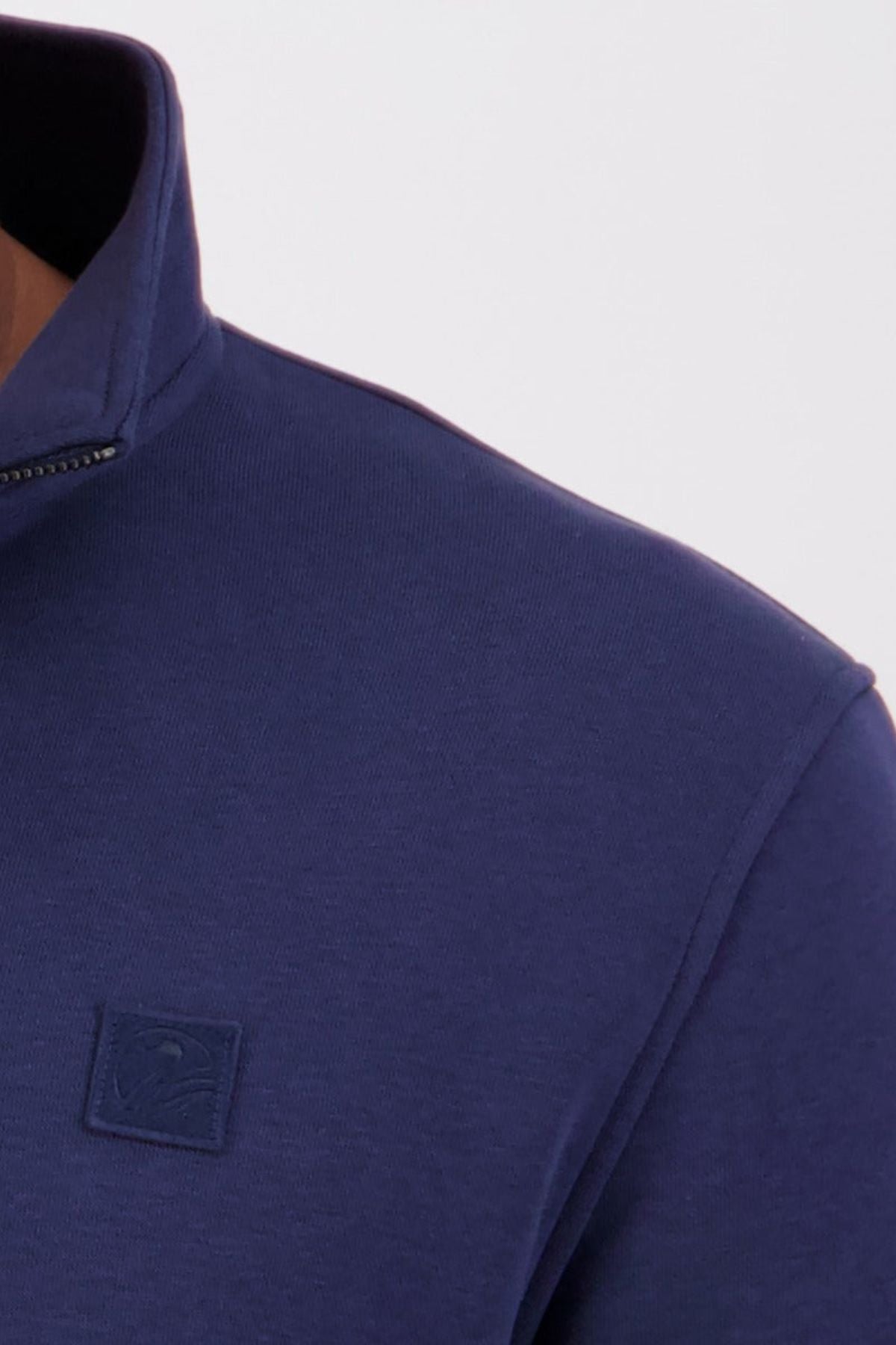 Close-up of a person wearing the Swanndri Fundamentals Quarter Zip in navy blue French Terry, featuring a small square embroidered logo on the chest. Only the shoulder, neck, and part of the collar are visible.