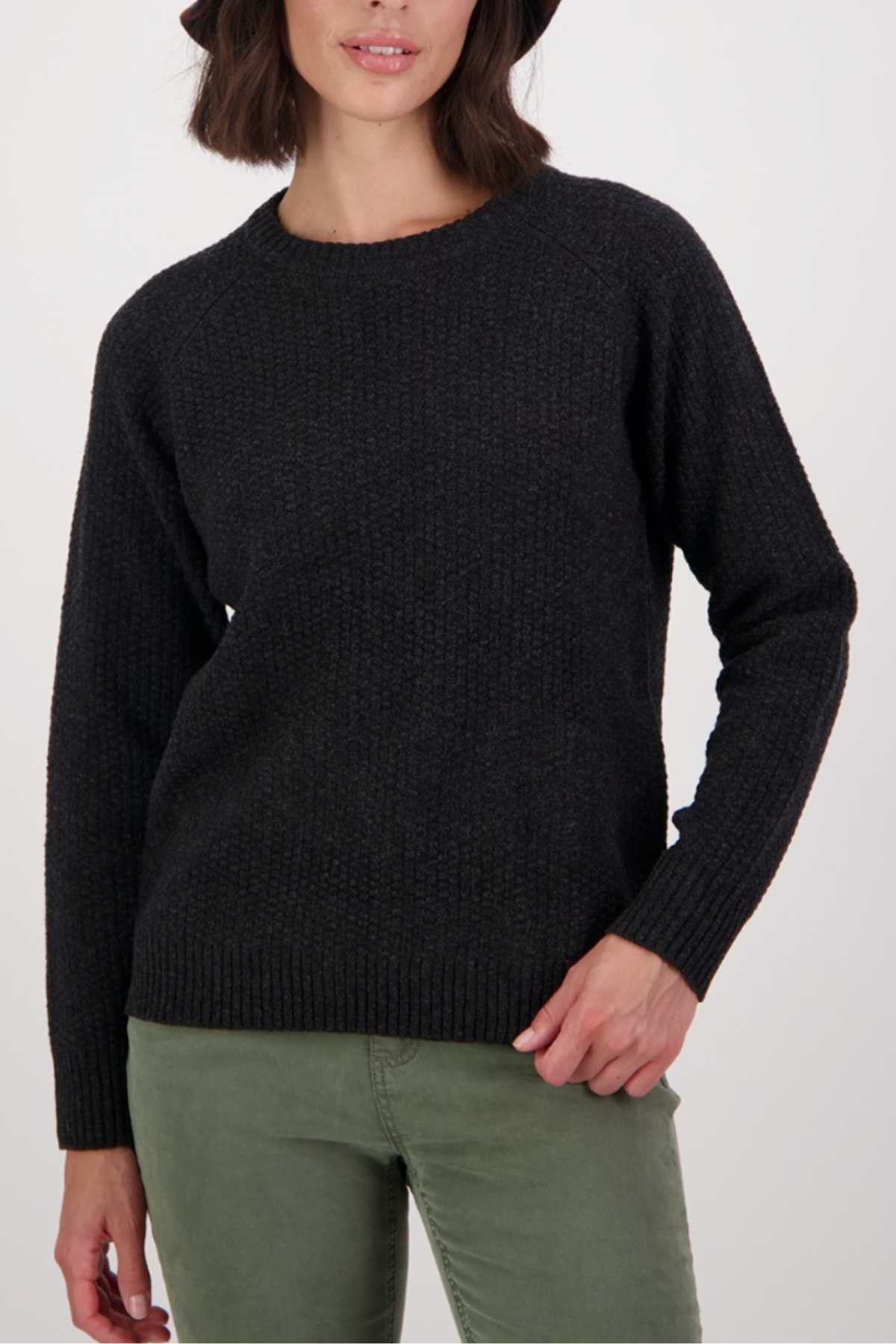 A woman wears the Swanndri Hayes Park Waffle Knit Crew with light green pants, standing against a plain light background, one hand on her hip and the other relaxed by her side.