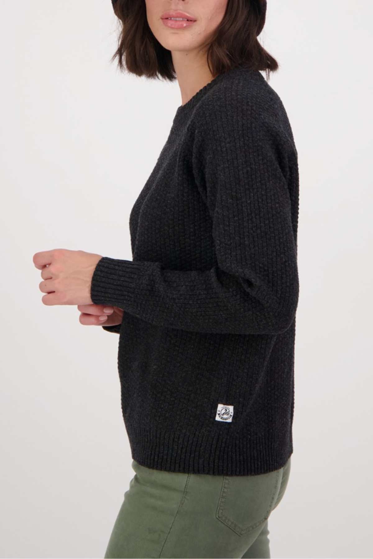 A woman with shoulder-length dark hair wears the Swanndri Hayes Park Waffle Knit Crew and olive green pants, standing sideways against a plain light background.