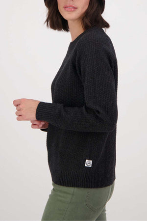 A woman with shoulder-length dark hair wears the Swanndri Hayes Park Waffle Knit Crew and olive green pants, standing sideways against a plain light background.